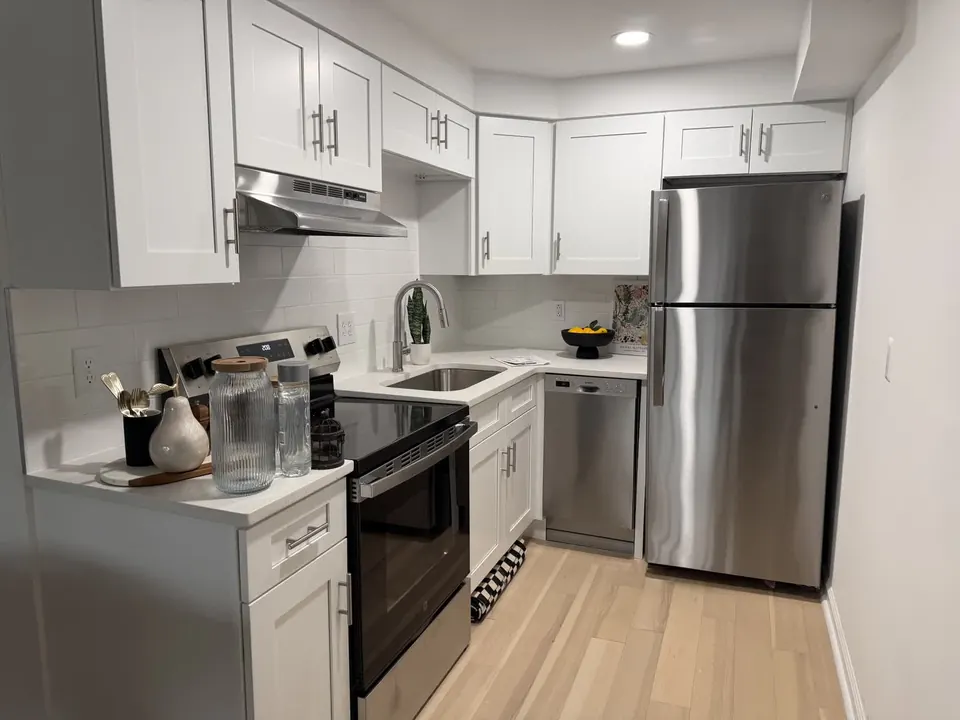 Completed apartment kitchen renovation with white cabinetry and stainless steel appliances